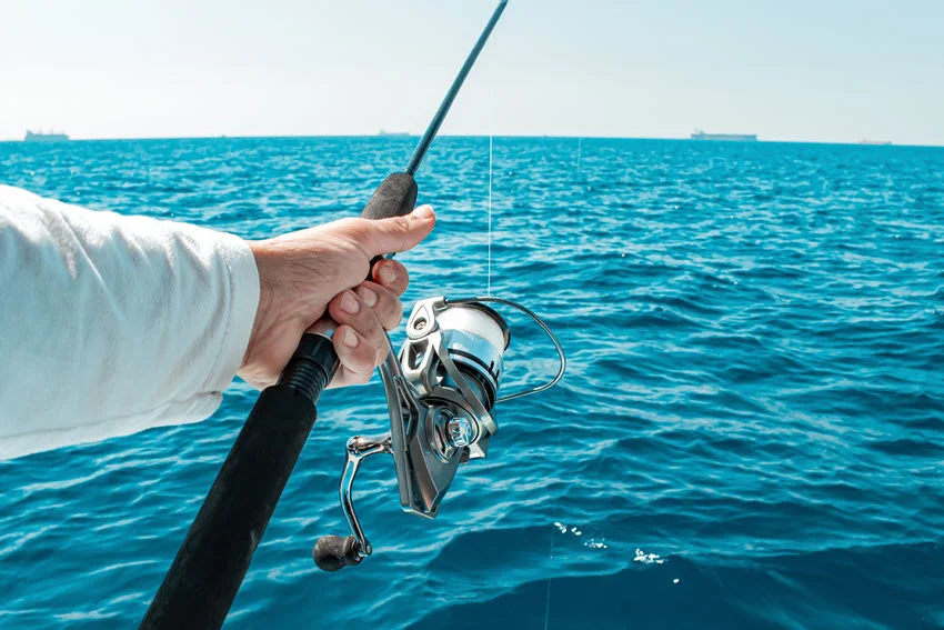 Close shot of an angler holding a spinning rod over open saltwater, a practical tackle visual for sections about gear, rod setups, and offshore Amberjack fishing techniques.