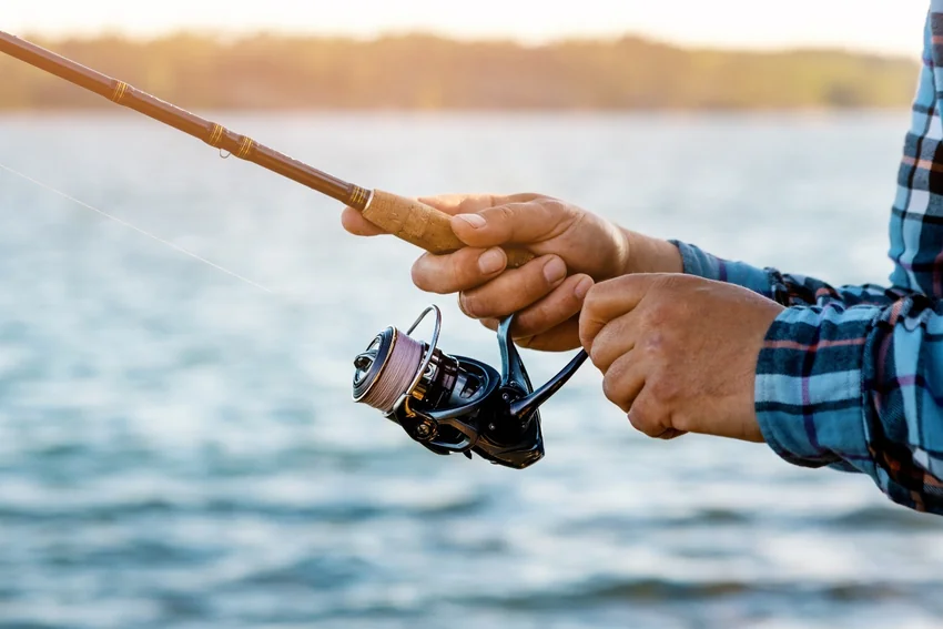 Close-up of an angler holding a cork-handled fishing rod and turning a spinning reel handle.