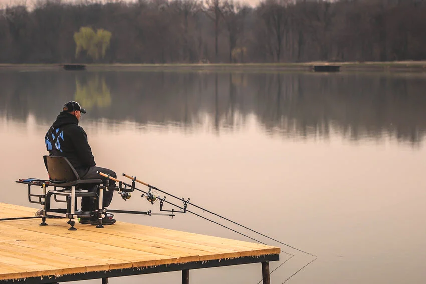 Wide shot of an angler fishing multiple rods from a dock, a common setup for Feeder fishing for Carp.