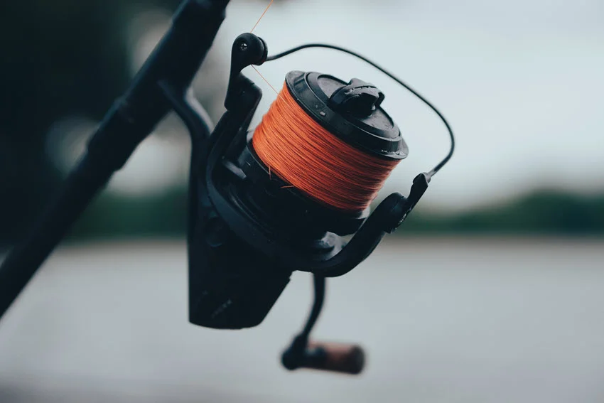Close-up shot of a fishing reel with an orange braided line, showcasing detailed components and vibrant color.