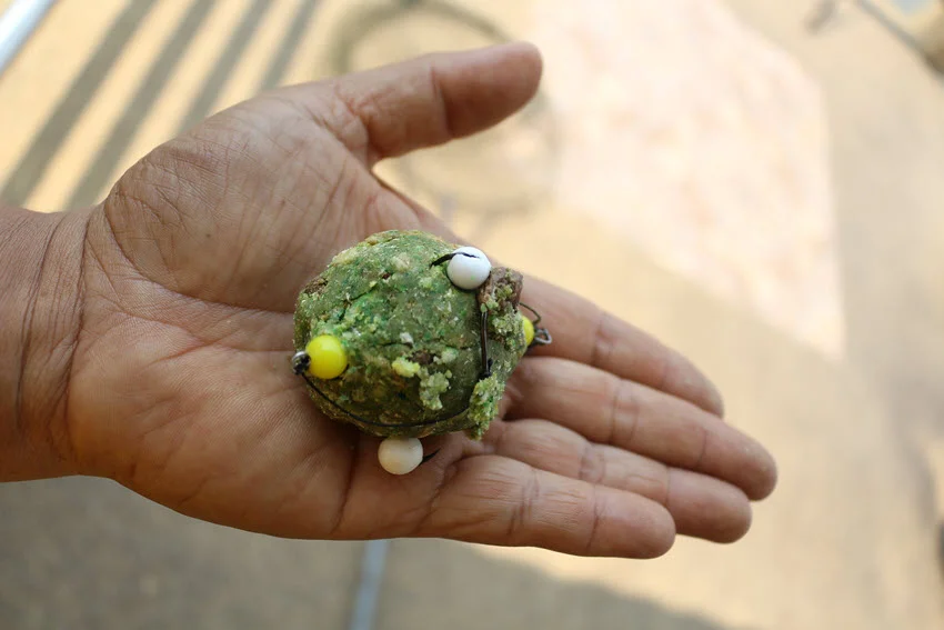 Close shot of an angler's hand holding green fishing bait holder hooks for stink bait, emphasizing the textured, odorous bait.