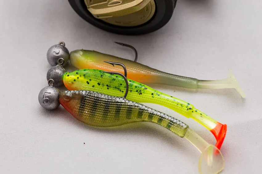 Close-up shot of rubber lures mounted on jig head fish hooks, isolated against a white background, showcasing their detailed design and bright colors.