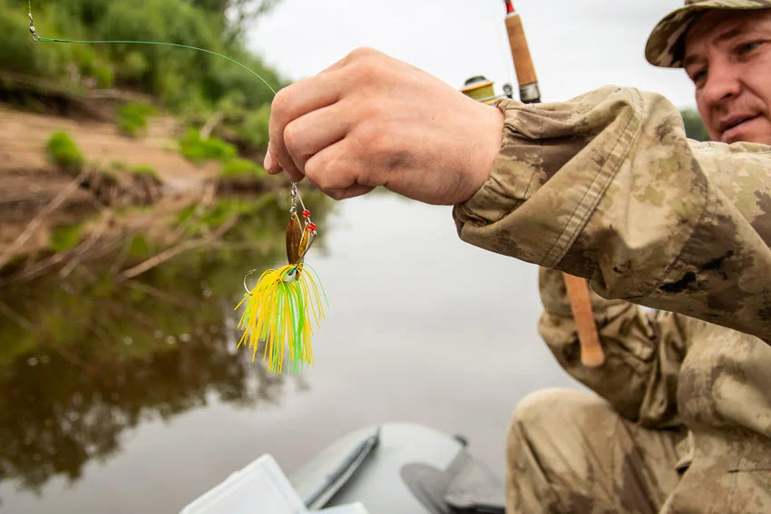 Close-up of a yellow fishing spinnerbait held in a fisherman’s hands, illustrating the lure’s design for summer fishing targeting predatory fish.