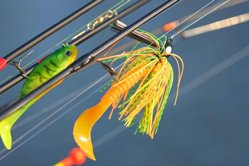Fishing spinning and casting rods with tackles on a pier, blurred lake background, selective focus on lines, bobber, and plastic jig with worm lures.