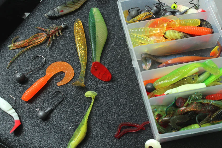 A spacious fisherman's tackle box packed with an extensive assortment of fishing gear, featuring soft bait lures, wobblers, poppers, jig heads, and hooks, all carefully arranged to provide quick access and readiness for any style of fishing.