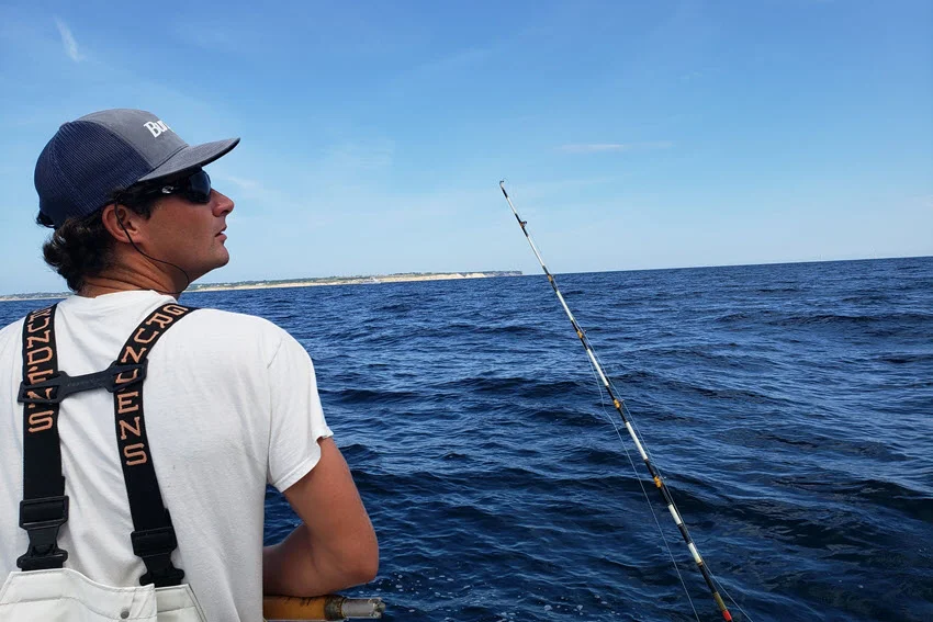 Back view of an angler on a charter boat wearing a hat and sunglasses while targeting Flounder over calm open water.