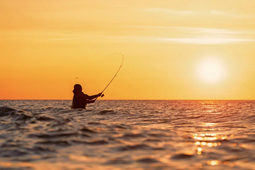View of an angler casting from shore during a calm sunset over the water.