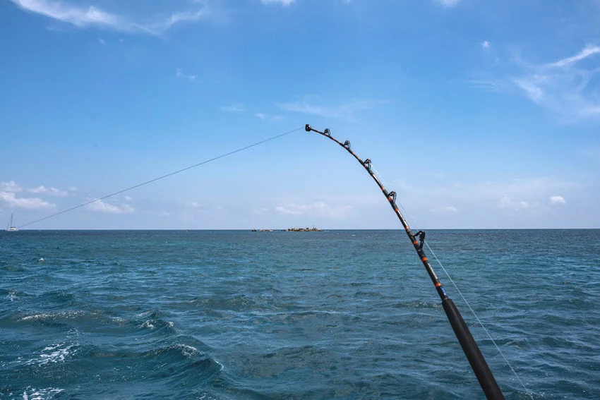 Bent offshore rod over reef water, showing the pressure and tackle strength needed when a Grouper digs back toward structure.