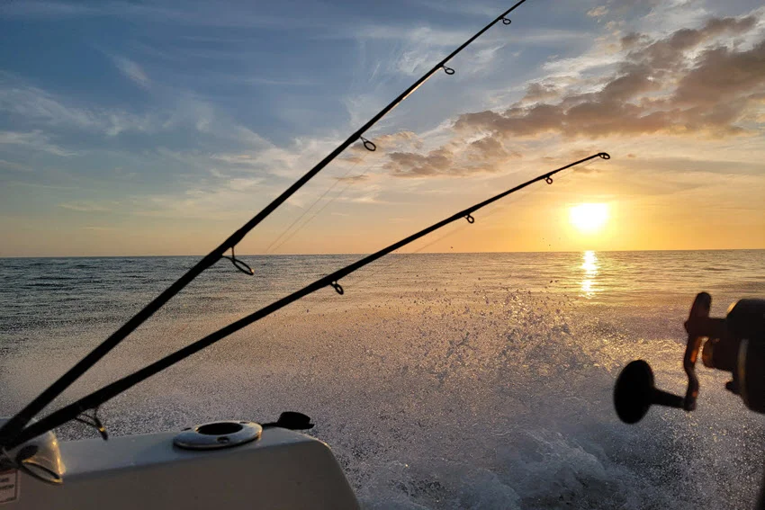 Offshore fishing charter running at sunrise with trolling rods out, showing the run toward deeper Grouper water and productive offshore structure.