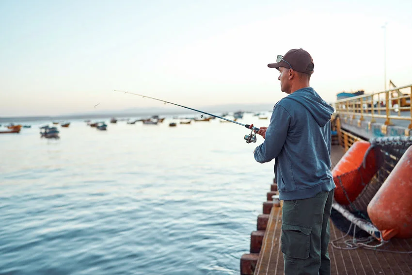 Focused shot of an angler fishing from a harbor pier, a practical position for casting Jack Crevalle lures around coastal structure.