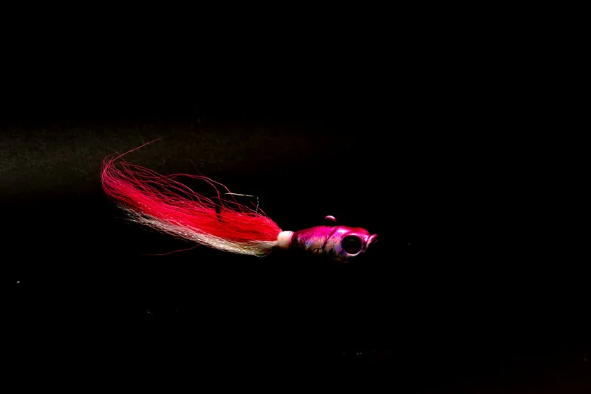 Focused shot of a pink bucktail jig against a dark background, showing the flowing hair and compact profile used for Jack Crevalle.