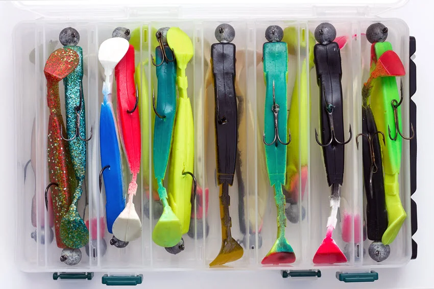 Top-down view of colorful soft plastic swimbaits stored in a tackle box for casting to Jack Crevalle in shallow coastal water.