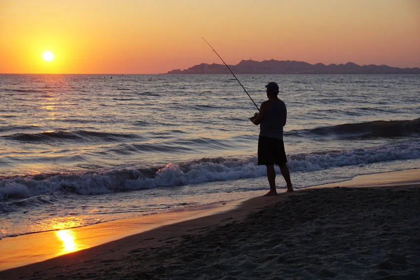 View of an angler surf fishing at sunset, casting beyond the breaking waves for Jack Crevalle feeding close to shore.