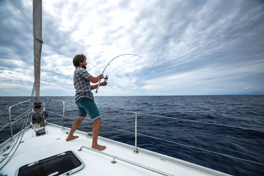 Action shot of an angler fighting a powerful fish from a sailboat in open water, illustrating the challenge of King Mackerel fishing.
