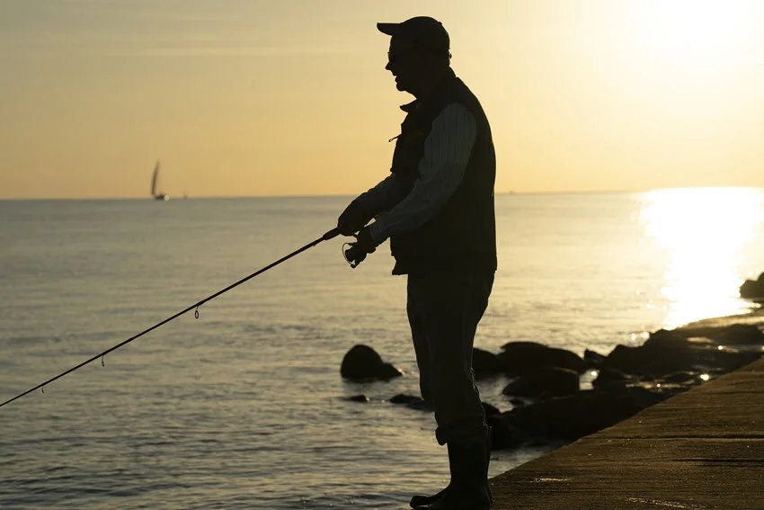 Silhouetted angler fishing beside calm coastal water at sunset, illustrating shore-based opportunities for targeting King Mackerel.