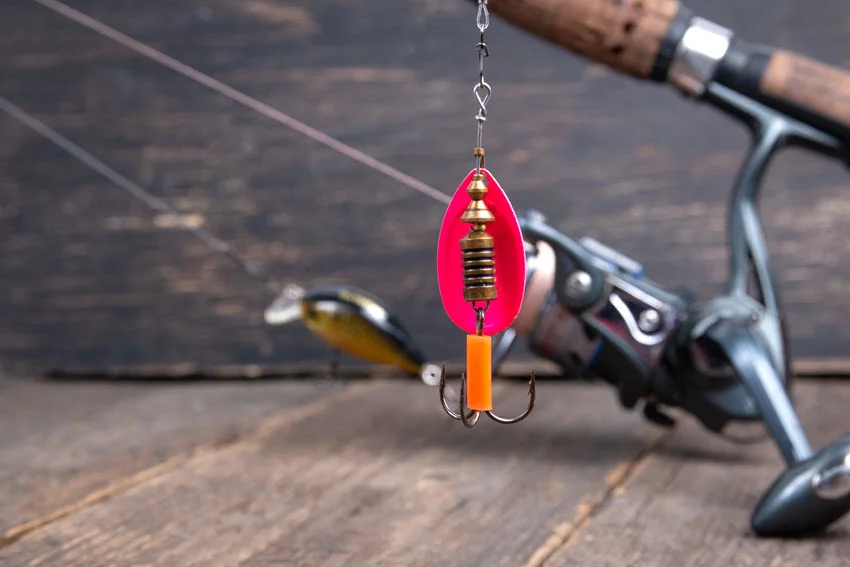 Focused shot of a bright inline spinner with a rotating blade and treble hook positioned beside a spinning rod and reel.