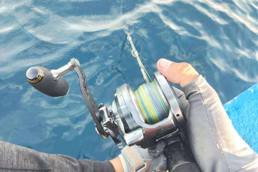 Angler dropping a jig during a slow pitch vertical jigging session, with the fishing line descending into the deep blue water.