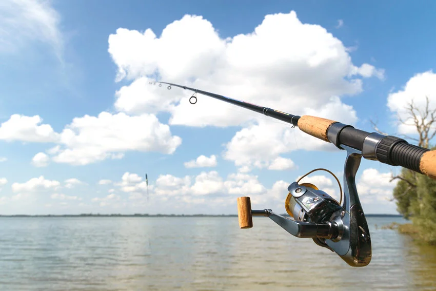 Spinning rod and reel pointed across open lake water, showing a versatile freshwater setup for casting Peacock Bass lures from shore or boat.