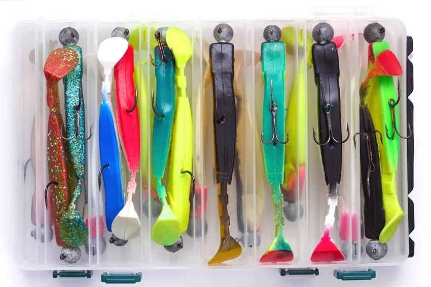 View of a tackle box filled with colorful soft plastic fishing lures rigged on jig heads, neatly arranged in separate compartments.