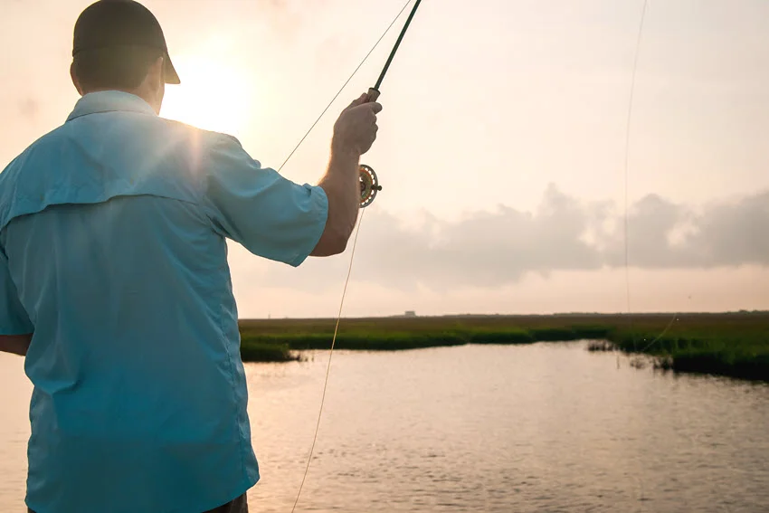 Angler fly casting across marsh water during low light, a productive window for targeting inshore fish.