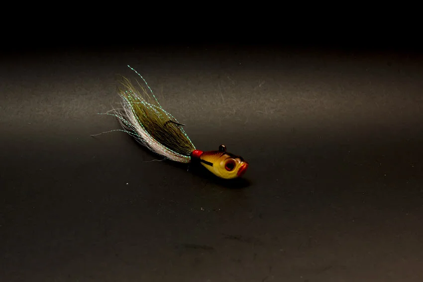 Bucktail jig with a flashing skirt on a dark background, showing a versatile Redfish lure for swimming, jigging, and working deeper cuts.
