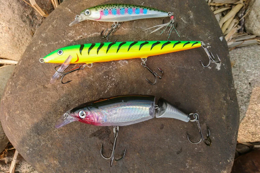Hard bait lures for Redfish fishing displayed on a rock, including minnow plugs, jerkbaits, and jointed swimbaits for covering shallow flats.