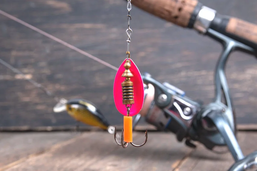 Inline spinner lure rigged near a spinning rod, showing a compact search bait that can create flash and vibration when fishing for Redfish.