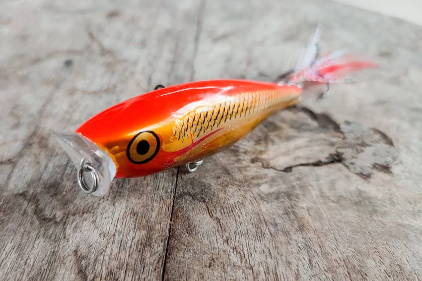 Orange topwater plug on weathered wood, showing a surface lure style used to trigger Redfish strikes over shallow flats and grass edges.