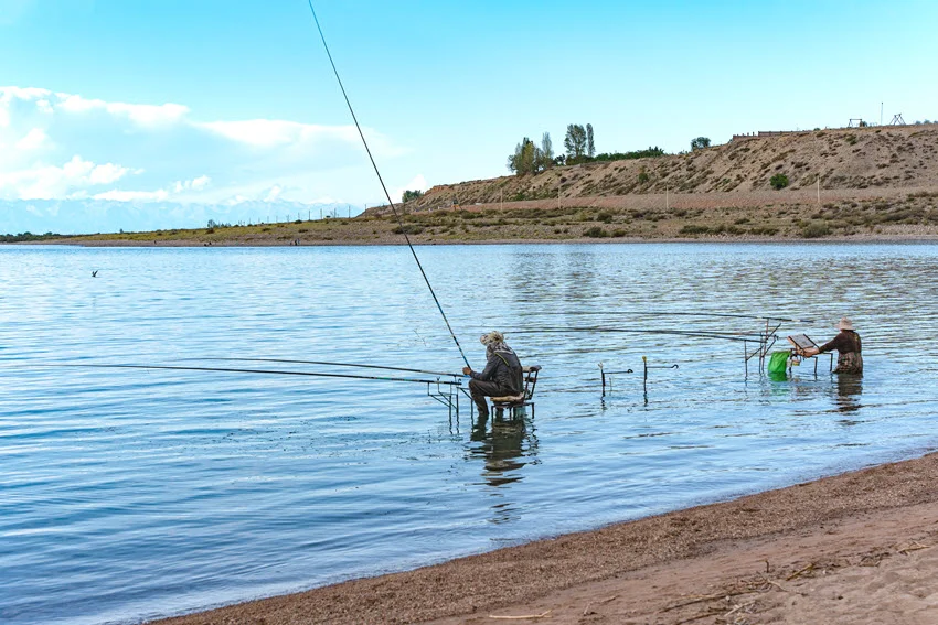 Shore anglers fishing calm water from a sandy bank, showing a simple land-based setup for casting lures near accessible inshore areas.