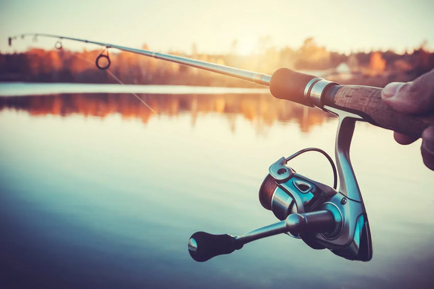 Spinning rod and reel pointed over calm water at sunset, showing a common setup for casting Redfish lures.