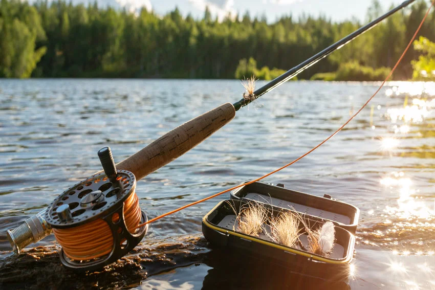 Fly fishing rod, reel, and Salmon flies beside the water, showing common lure-style gear used for targeting Salmon in rivers and clear freshwater areas.