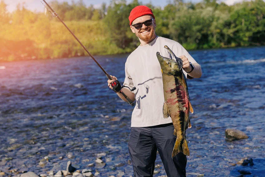 Angler holding a Salmon beside a river after a successful catch, showing how lures and flies can work through productive current and holding water.