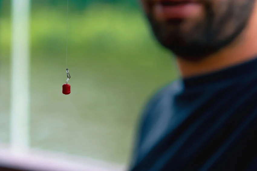 Close-up color bait for fish on a line and on a hook, held by angler in a blurry background.