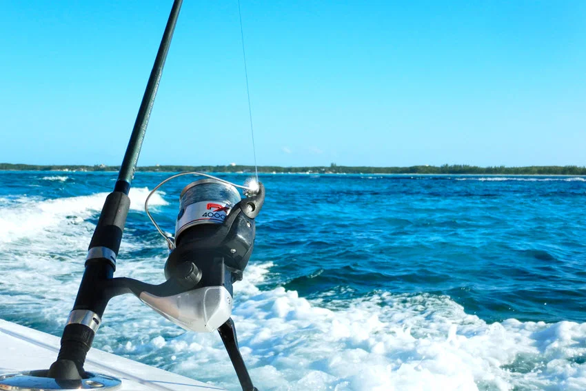 Close-up of a fishing rod and reel on a moving boat with sea and sky blurred in the background.