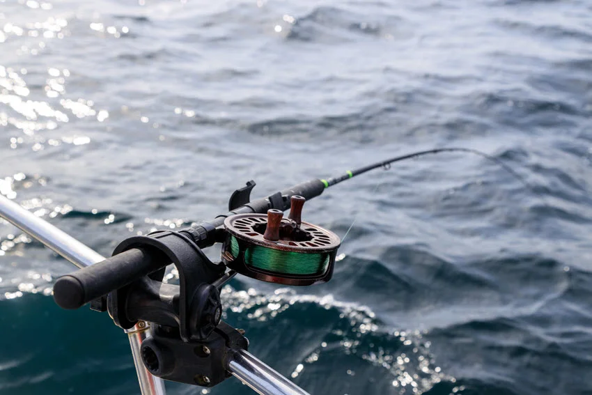 Fishing rod and reel holder attached to a moving boat, with line casted into deep ocean water.