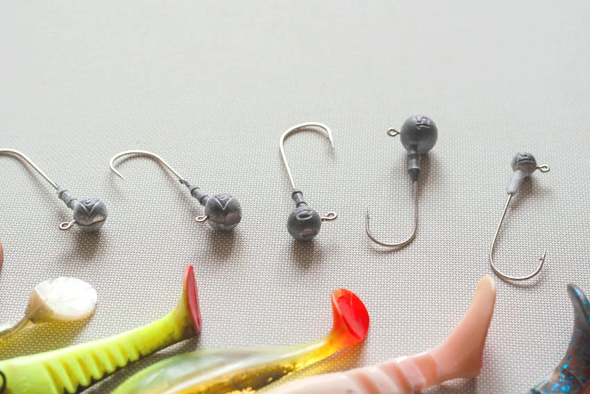 Random jig heads and fragments of rubber lures lie on a white textured background.
