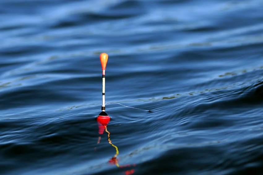 Focused shot of an orange and white float bait drifting on the ocean surface.