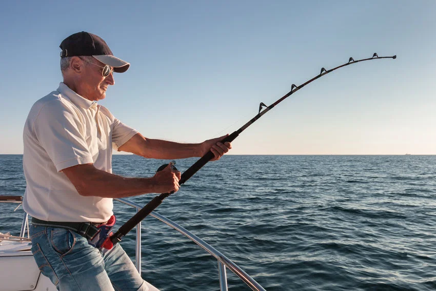 Action shot of an angler fighting a powerful fish with heavy tackle from a boat on open coastal water.