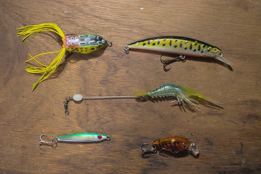 Assortment of artificial fishing lures, including minnow plugs, a shrimp imitation, and small hard baits considered for Sheepshead fishing.