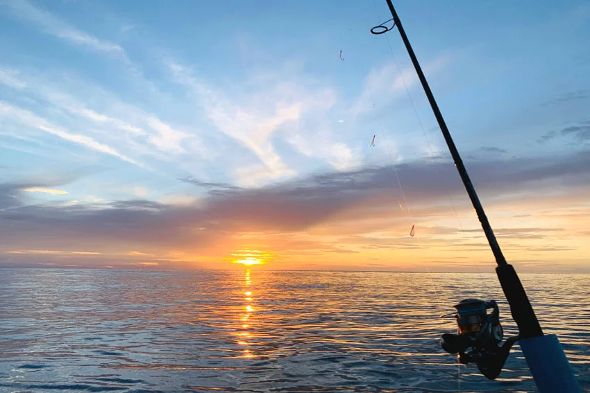 Fishing rod resting on a charter boat at sunset with calm waves in the background.
