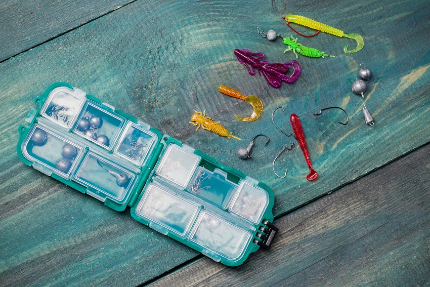 Collection of colorful jigs and soft plastic lures arranged beside a small tackle box.