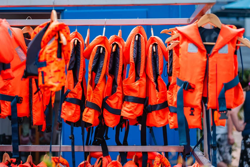 Bright orange life jackets neatly arranged on a rack at a rental station.