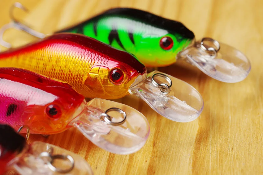 Three minnow wobblers, in pink and green color placed on a wooden surface.