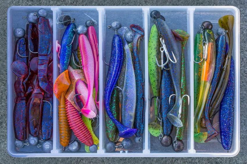 Plastic lures of different sizes and colors are placed in plastic containers.