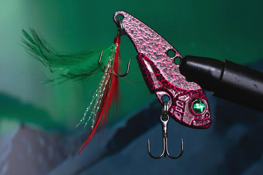 Focused shot of a red crankbait with a hanging circle hook and green feathers.