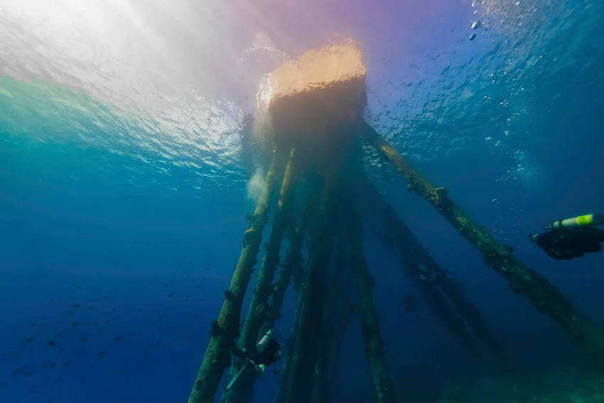 Underwater view of a saltwater pier with a scuba divers swimming.