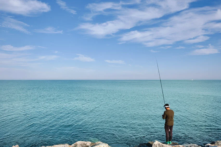 Angler fishing from a rocky saltwater shoreline, showing a common land-based setup for targeting Snook around open coastal water and structure.