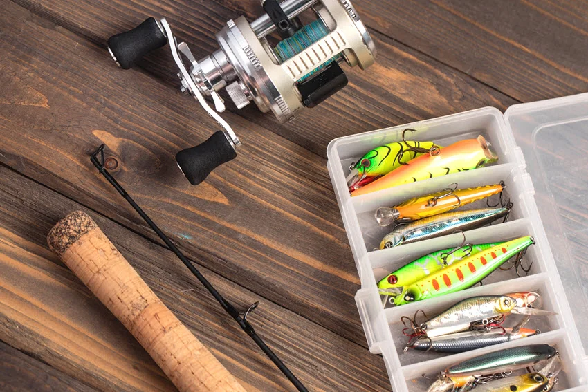 Casting rod and reel with a tackle box of twitching lures on a wooden surface, showing hard bait options for working Snook around structure, current, and shallow edges.