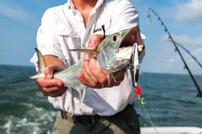 Angler holding a Spanish Mackerel caught on a reflective metal spoon while fishing from a boat in open coastal water.