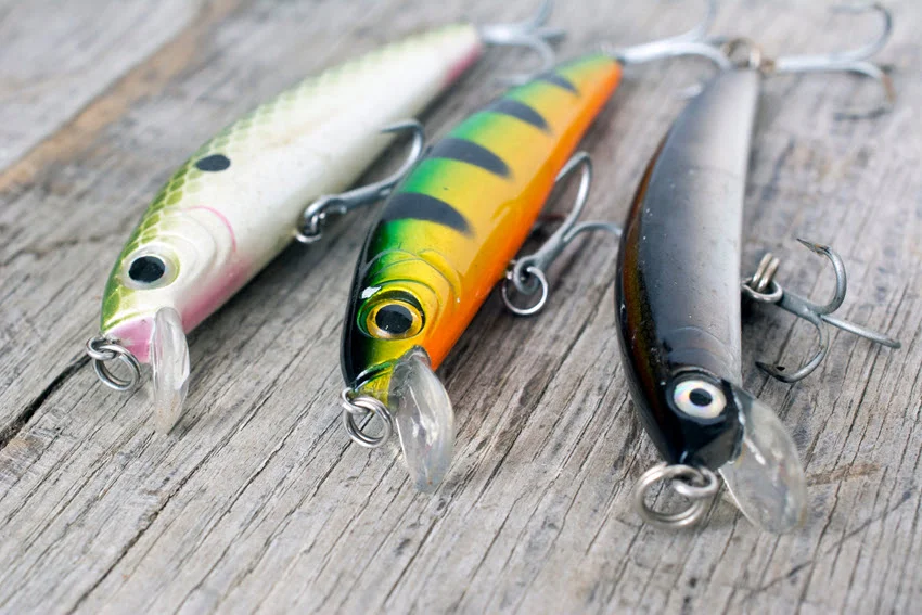 Close view of three minnow-style hard lures with treble hooks, suitable for casting or trolling for fast-moving Spanish Mackerel.